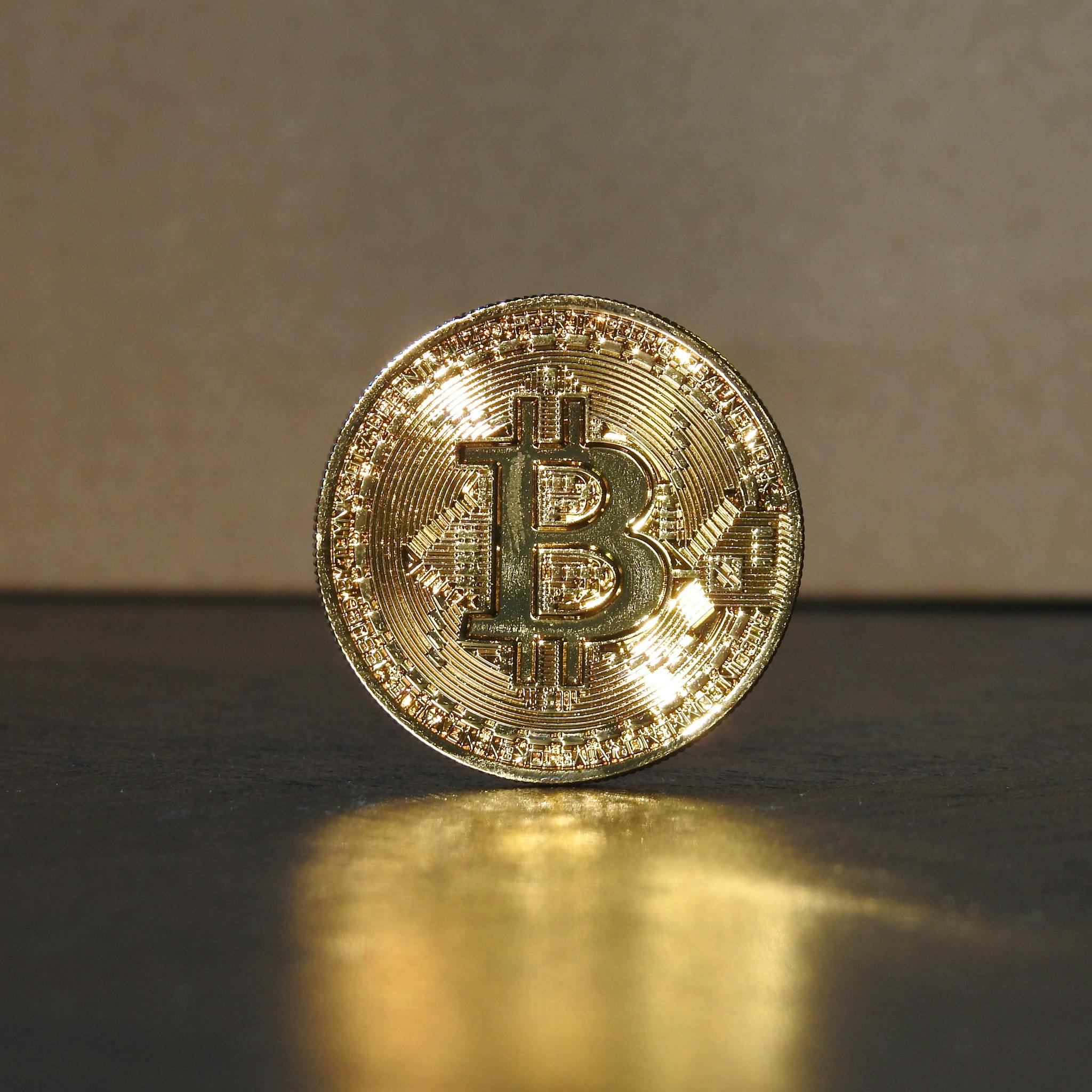 A shimmering golden Bitcoin coin standing upright on a reflective surface, illuminated by warm light.