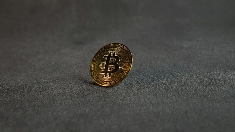 Close-up image of a golden Bitcoin standing on a grey surface, symbolizing cryptocurrency and digital finance.