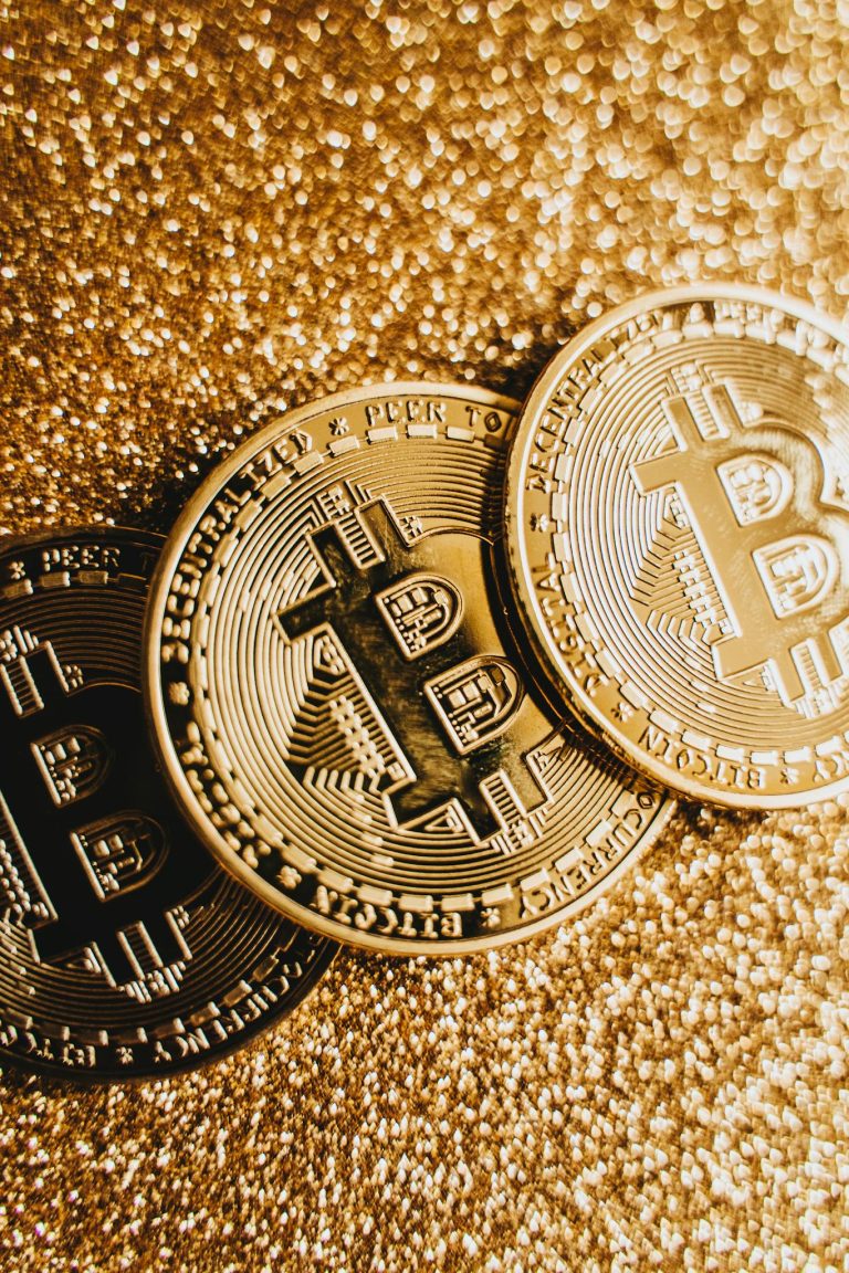 Three Bitcoin coins on a sparkling gold surface, symbolizing digital currency.